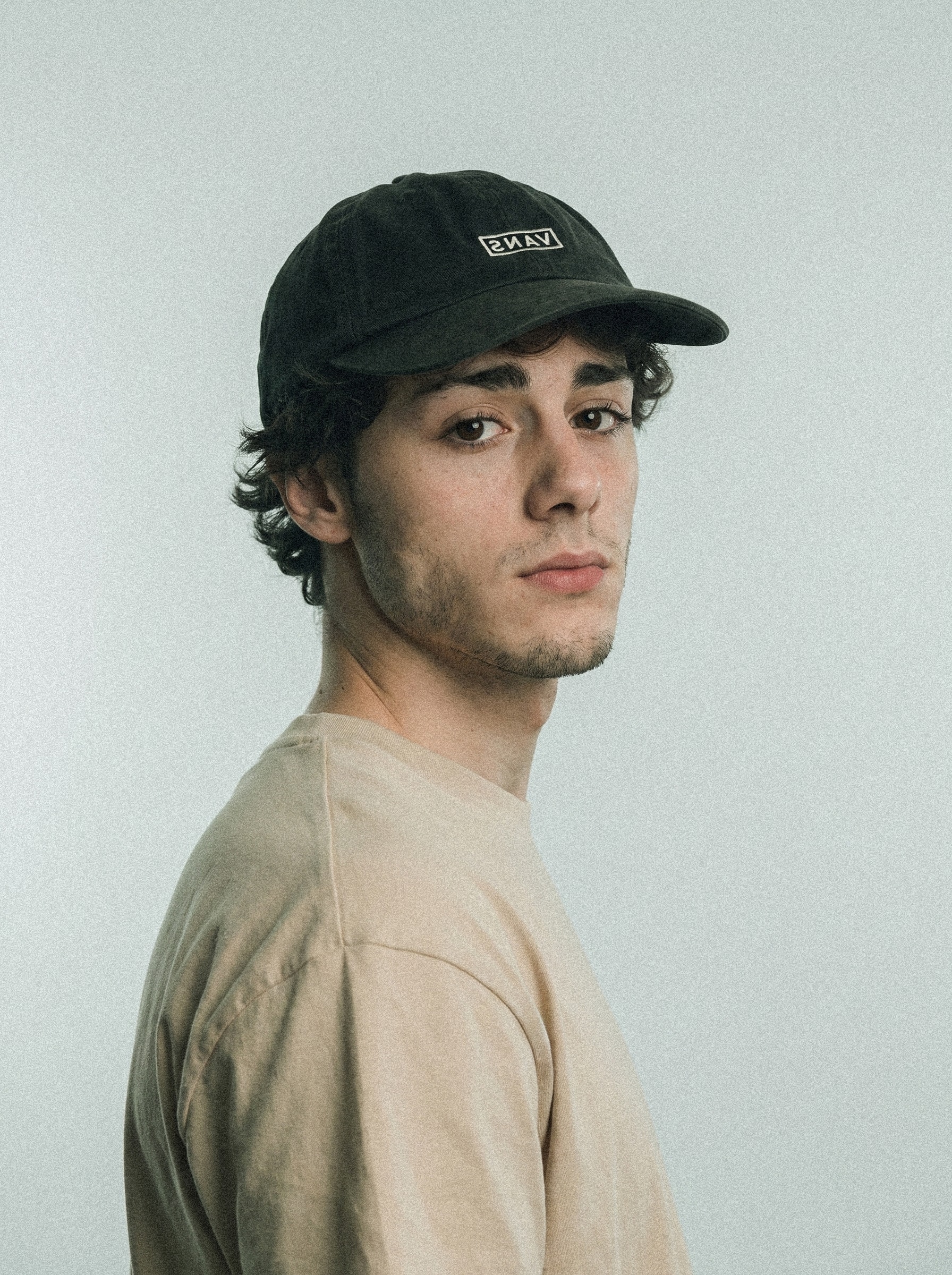 Retrato de Facundo con gorra negra y remera clara sobre fondo gris.